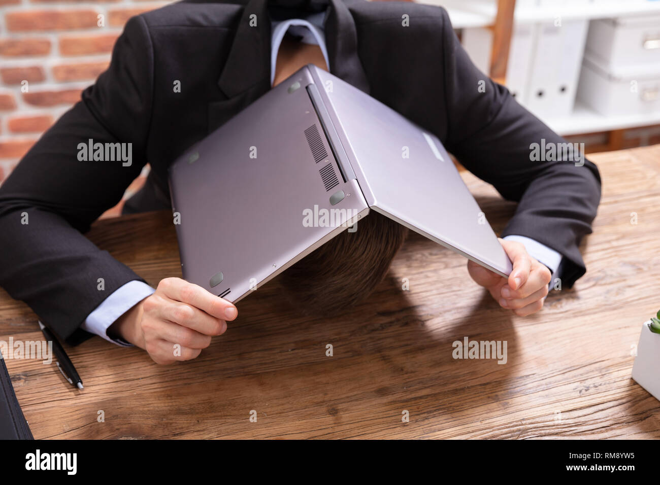Un homme d'affaires couvrant la tête avec un ordinateur portable sur le bureau au lieu de travail Banque D'Images