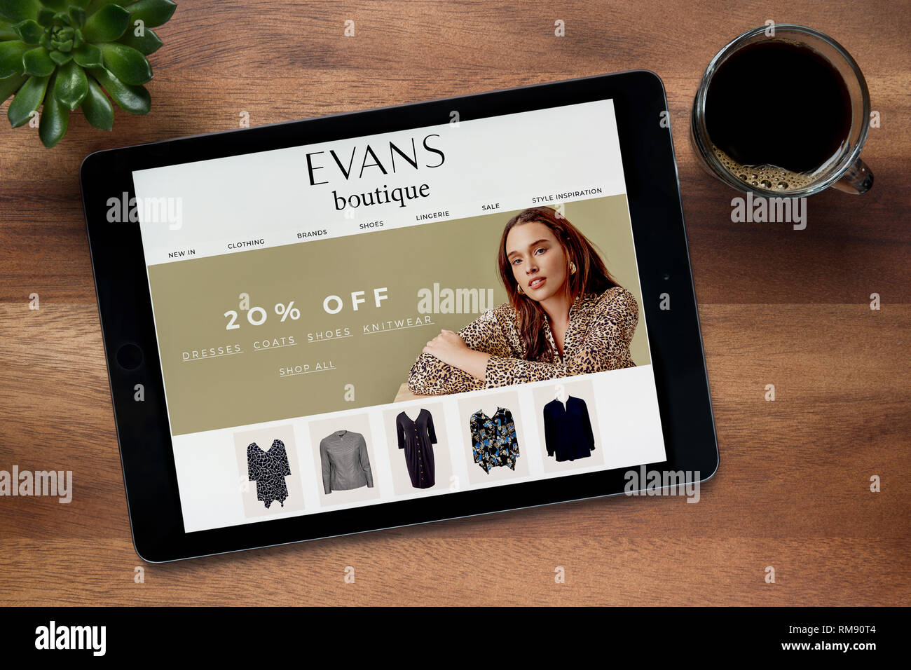 Le site web de Boutique Evans est vu sur un iPad tablet, sur une table en bois avec une machine à expresso et d'une plante (usage éditorial uniquement). Banque D'Images