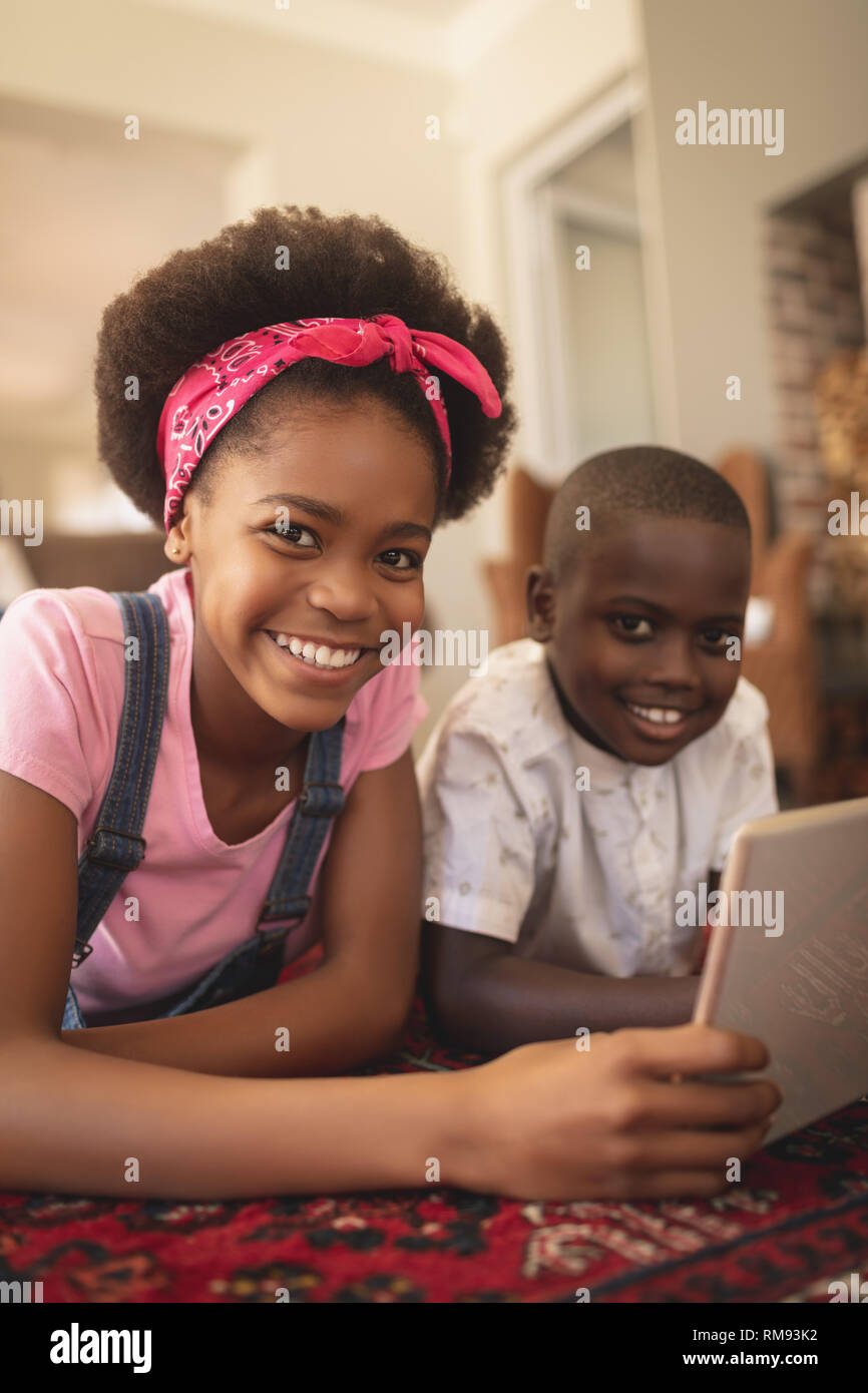 Happy African American sœur lying on floor with digital tablet and looking at camera Banque D'Images