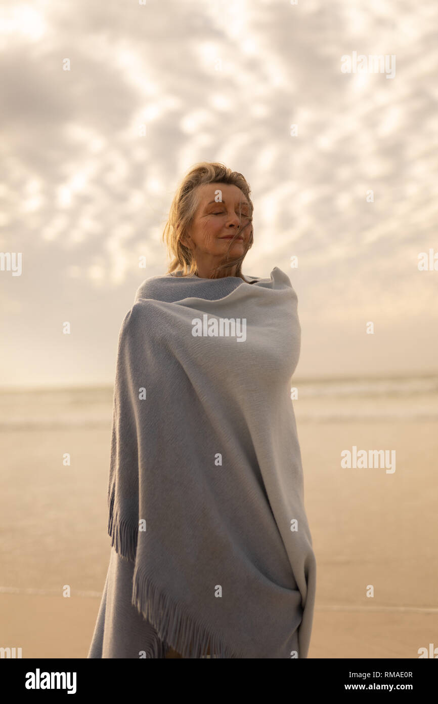 Hauts femme enveloppée dans un châle avec les yeux fermés debout sur la plage Banque D'Images