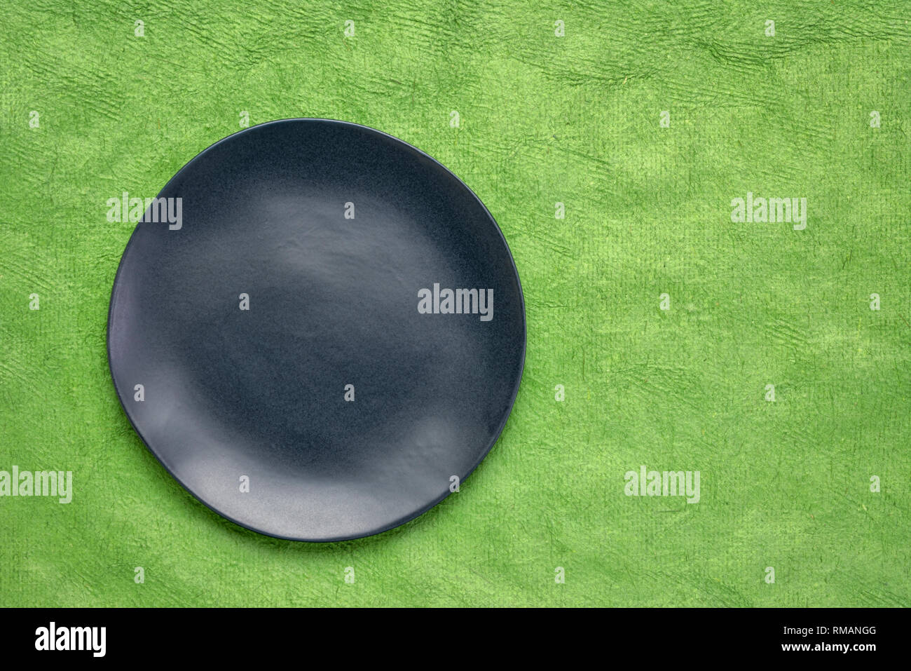 Plaque en céramique noire avec un bord irrégulier sur un papier fait main verte Maya Huun avec une copy space Banque D'Images