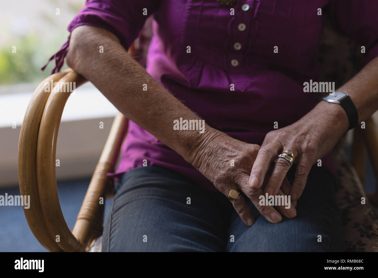 Senior woman with mains jointes sur ses genoux à la maison Banque D'Images