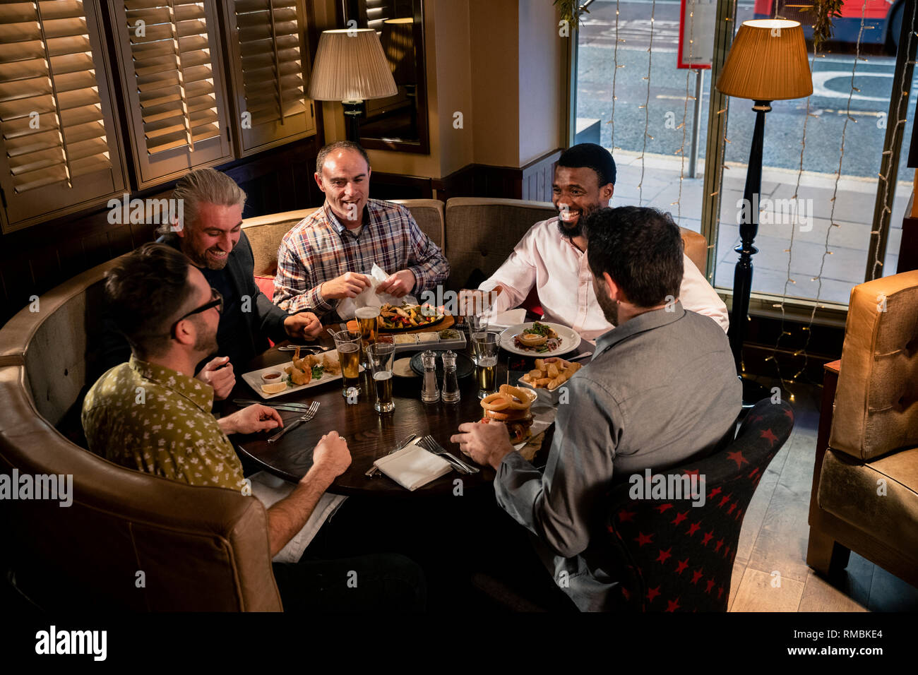 Groupe d'hommes déjà assis à la table dans un restaurant. Ils profitent de la nourriture, parler et rire. Banque D'Images