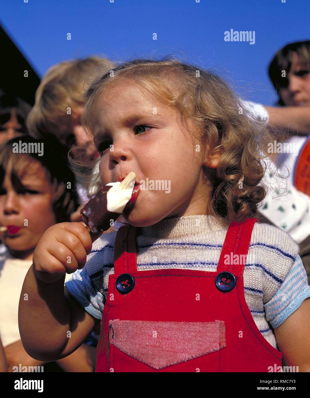 Une petite fille mange une glace avec gourmandise. Banque D'Images