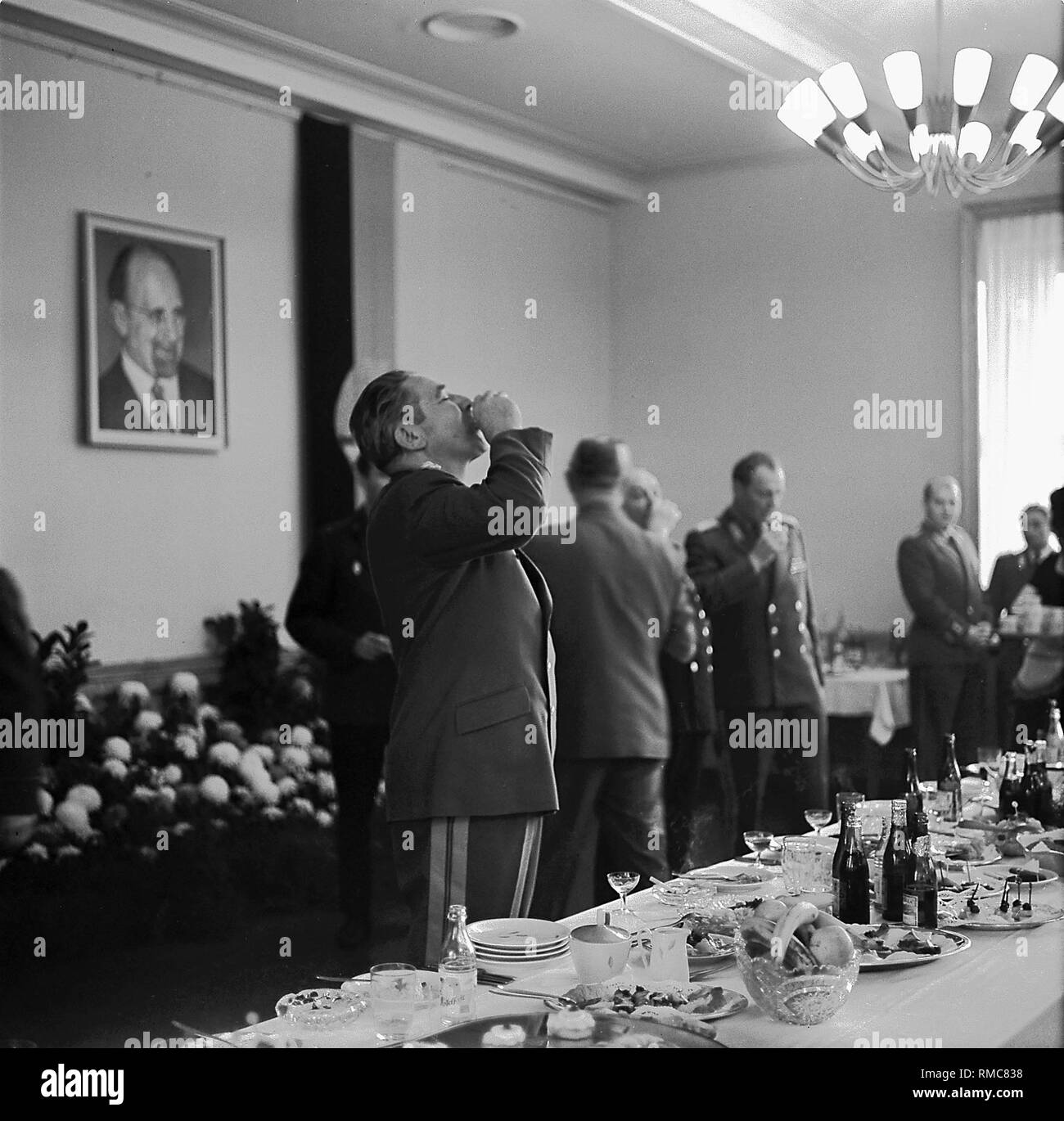 Le ministre de la défense de la RDA et de l'ANV Heinz Hoffmann déplace un schnaps. Derrière lui pend un portrait de Walter Ulbricht. Banque D'Images