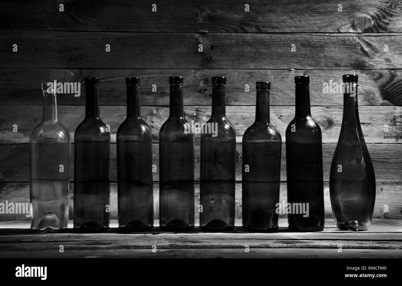 Vieilles bouteilles de vin dans le noir sur une table de bois en noir et blanc. Banque D'Images