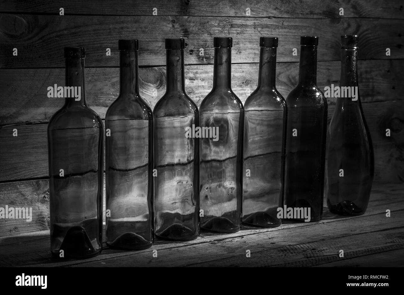 Vieilles bouteilles de vin dans le noir sur une table de bois en noir et blanc. Banque D'Images
