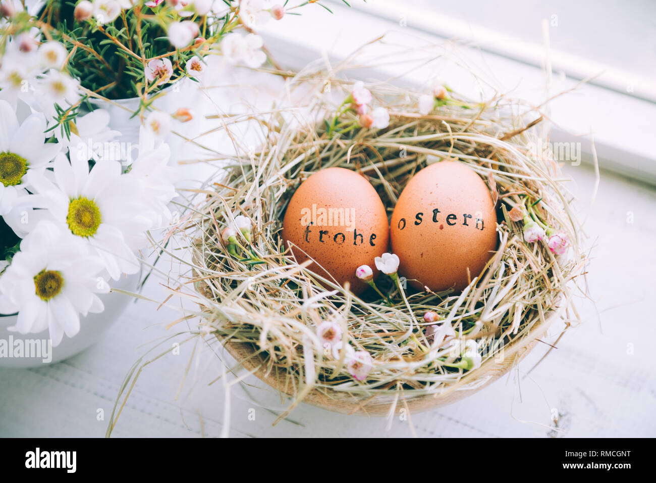 Les oeufs de Pâques avec des timbres en caoutchouc 'Frohe Ostern" message d'un texte dans un nid de foin et de fleurs à côté d'une fenêtre à la maison Banque D'Images