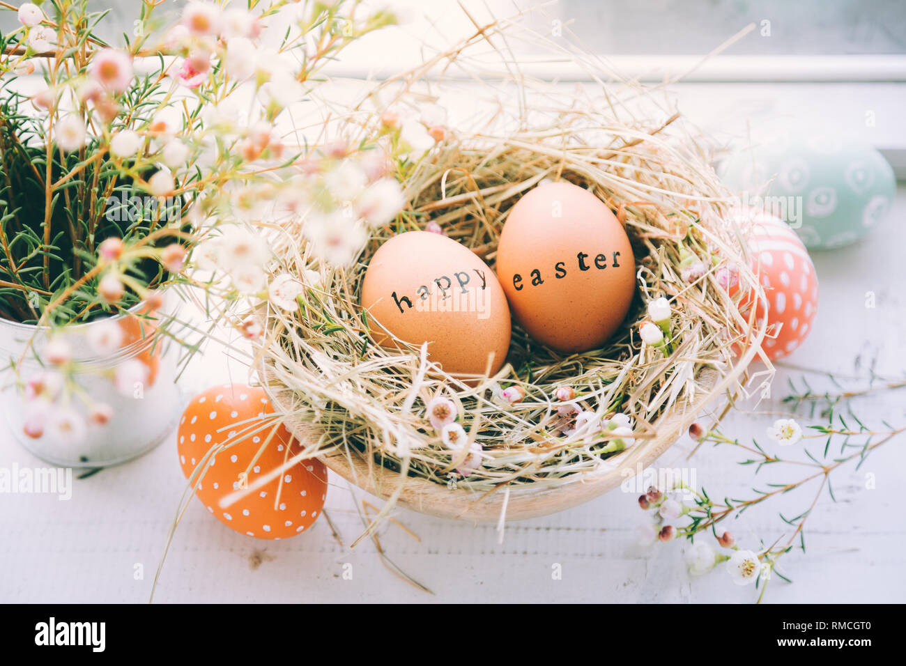Les œufs de pâques avec tampon de caoutchouc Joyeuses Pâques texte d'accueil dans un nid de foin et de fleurs à côté d'une fenêtre à la maison Banque D'Images