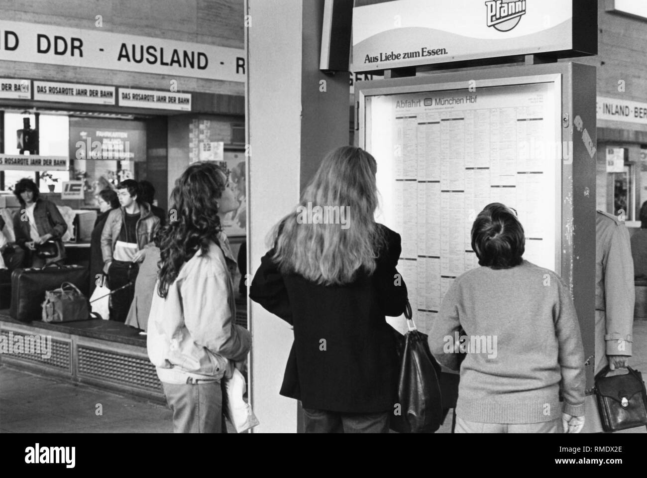 Trois femmes sont debout en face d'un calendrier à la Munich Hauptbahnhof (gare principale). Dans l'arrière-plan, un bureau de vente de billets. Le calendrier ci-dessus la publicité de l'Pfanni GmbH & Co. OHG. Banque D'Images