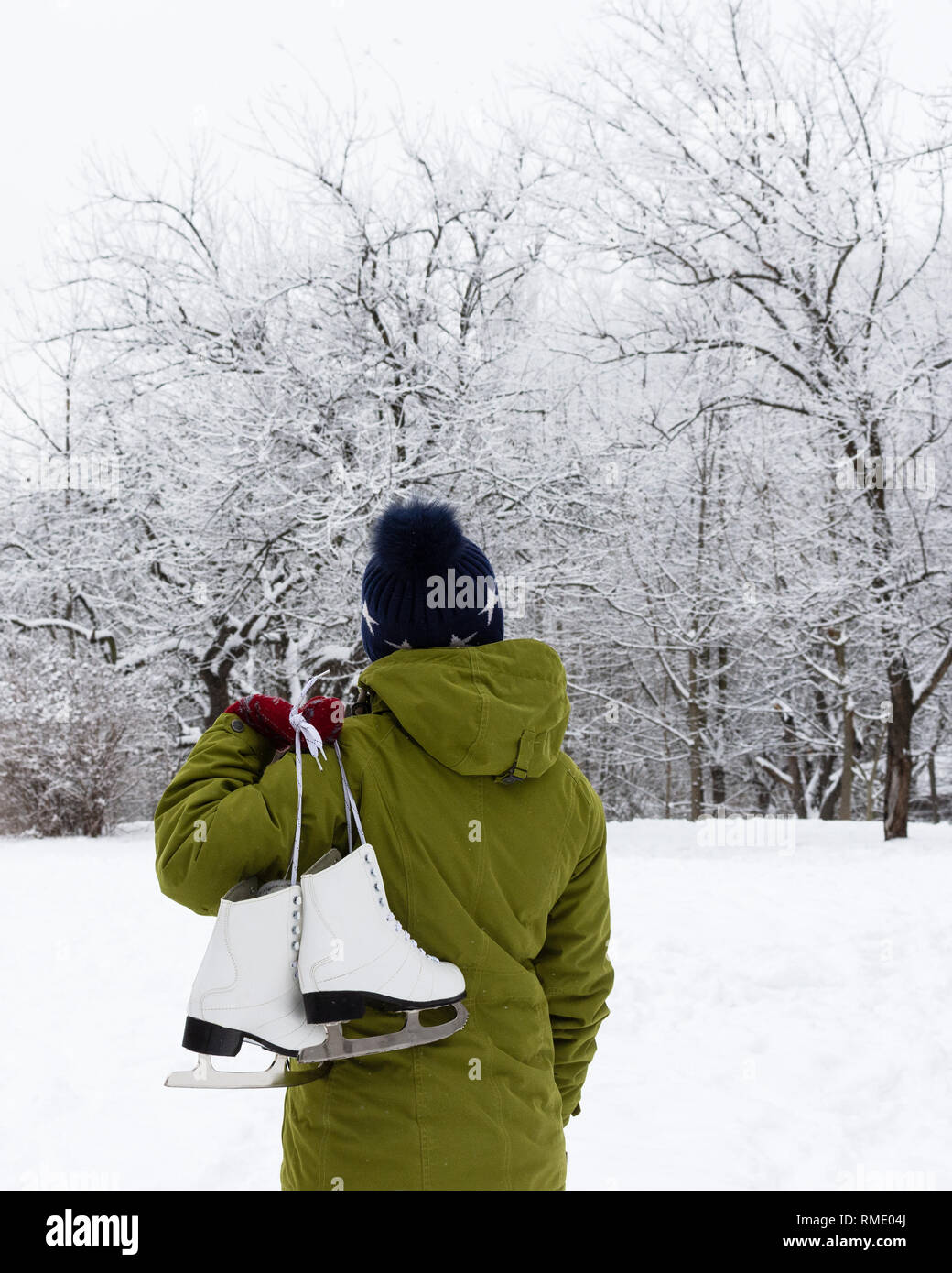 Femme dans une veste verte avec des patins à glace sur l'arrière-plan d'un paysage d'hiver Banque D'Images
