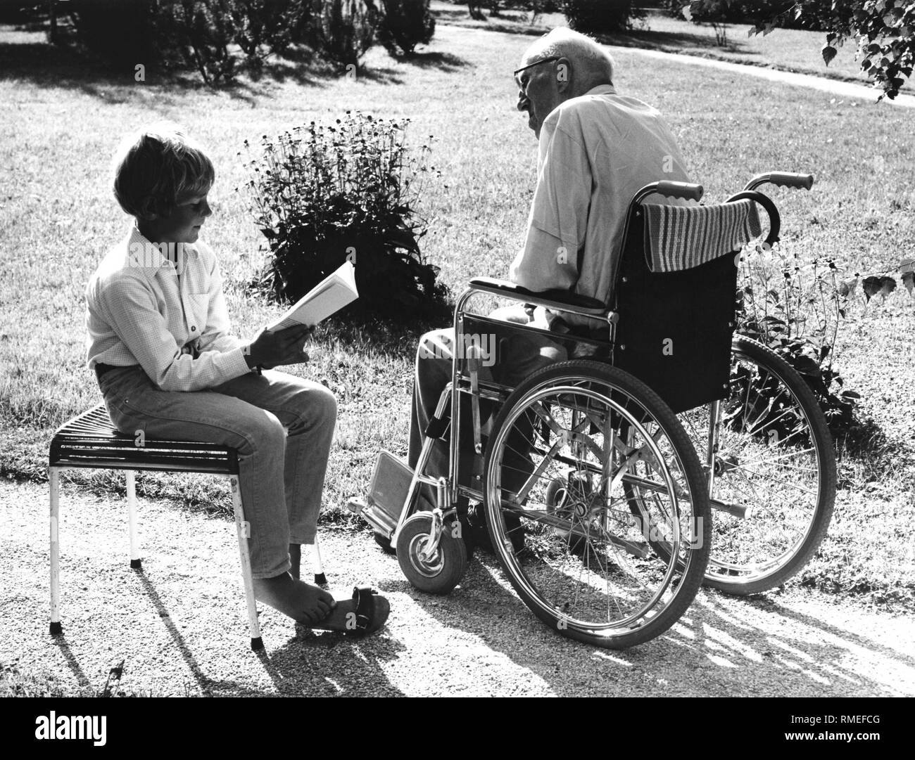 Enfant qui visite un vieil homme en fauteuil roulant, 1970 Banque D'Images