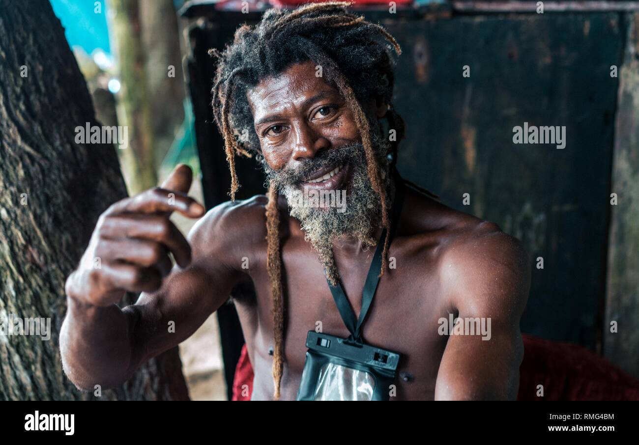 African American male barbu avec des dreadlocks et levé les mains de fumer un cigare à proximité d'arbres Banque D'Images