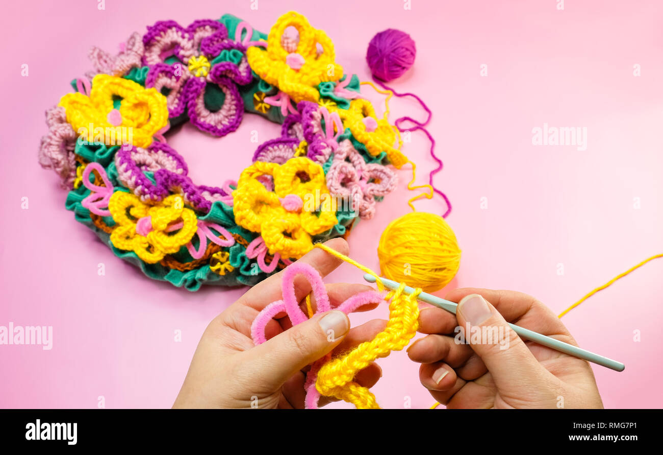 Crochet fleurs mains. Pour l'élaboration de simple fil de laine jaune et rose nettoie-pipe. Une femme l'élaboration d'un format de guirlande. Banque D'Images