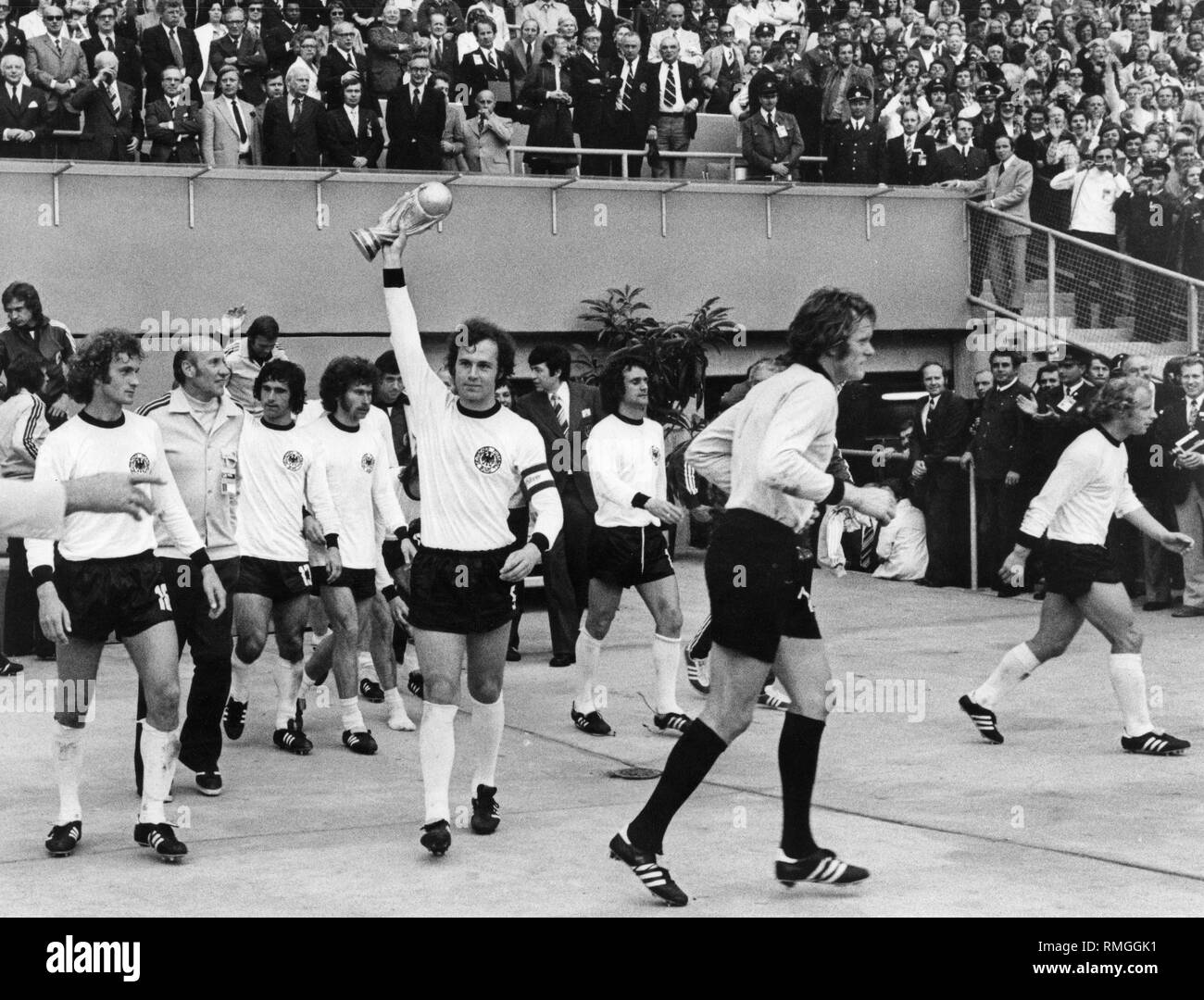 Franz Beckenbauer détient le trophée de la Coupe du monde en tant que capitaine de l'équipe nationale de football allemande, après la victoire finale 2-1 au-dessus de la Hollande. À l'extrême droite est son coéquipier Berti Vogts. Banque D'Images