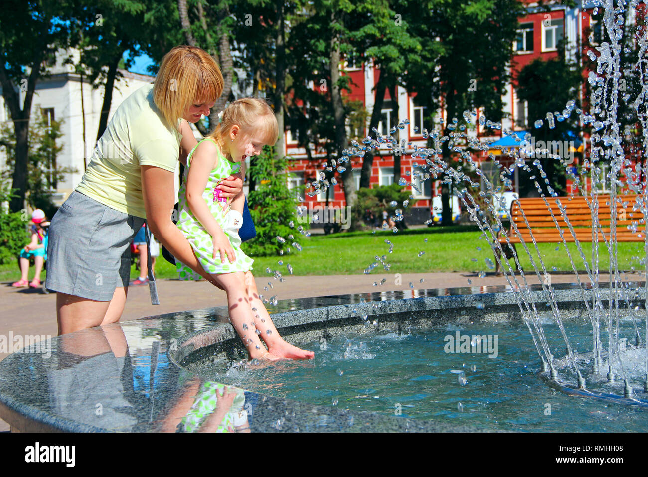 Mère et sa fille jouant près des fontaines de la ville en parc. Mère de sa fille, laver les pieds en fontaines. Circuit de refroidissement par temps chaud. Drôle de week-end Banque D'Images