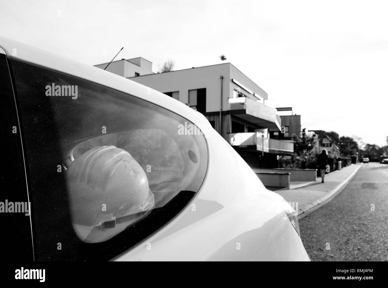 Casque de sécurité pour la construction vu sur le siège arrière d'une voiture blanche avec ingénieur silhouette féminine prépare à visiter l'immeuble fini - noir et blanc Banque D'Images