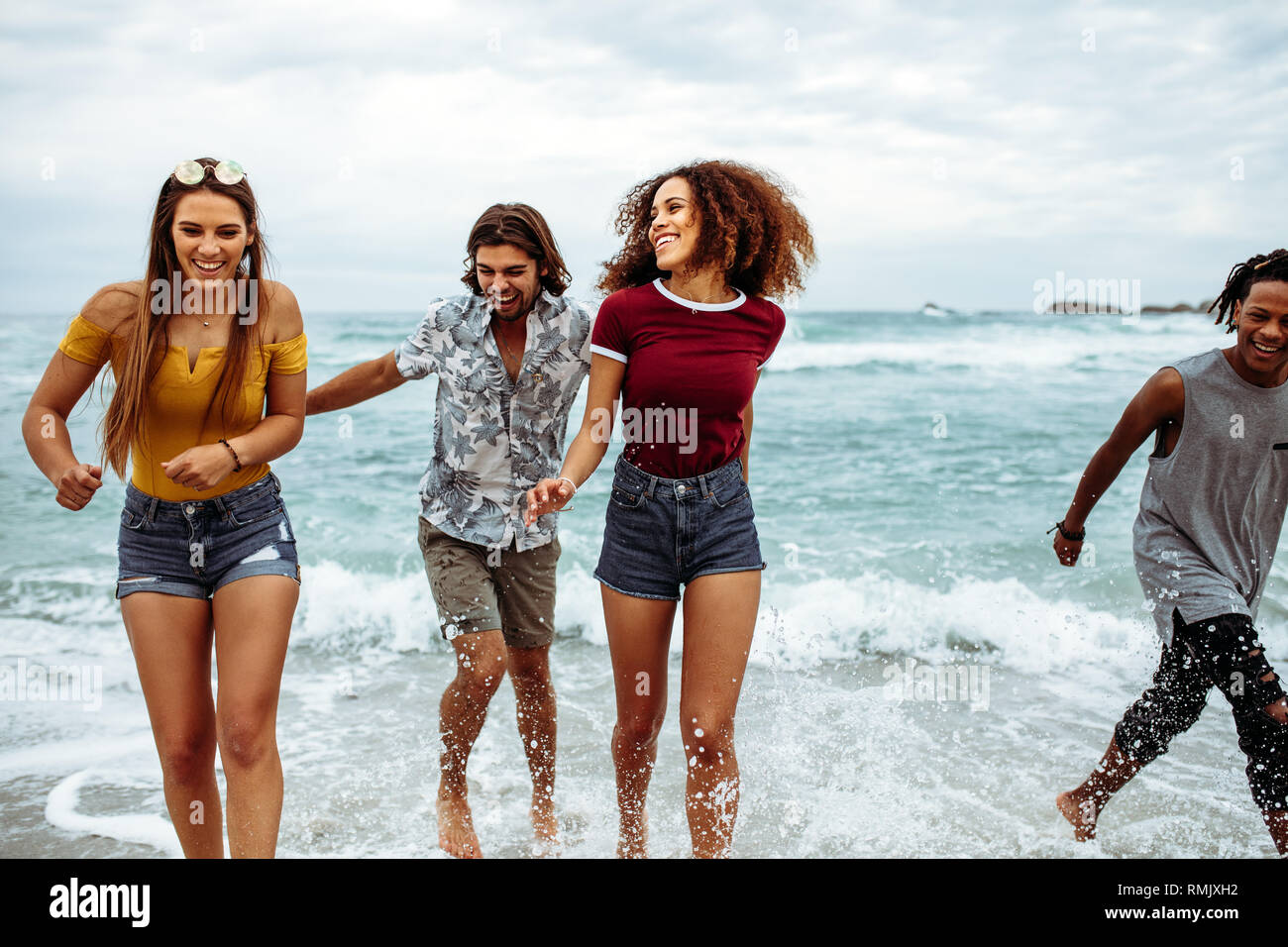Les hommes gais et les femmes la marche sur la plage. Les jeunes hommes multi-ethnique et les femmes marcher sur mer ayant beaucoup de plaisir. Banque D'Images