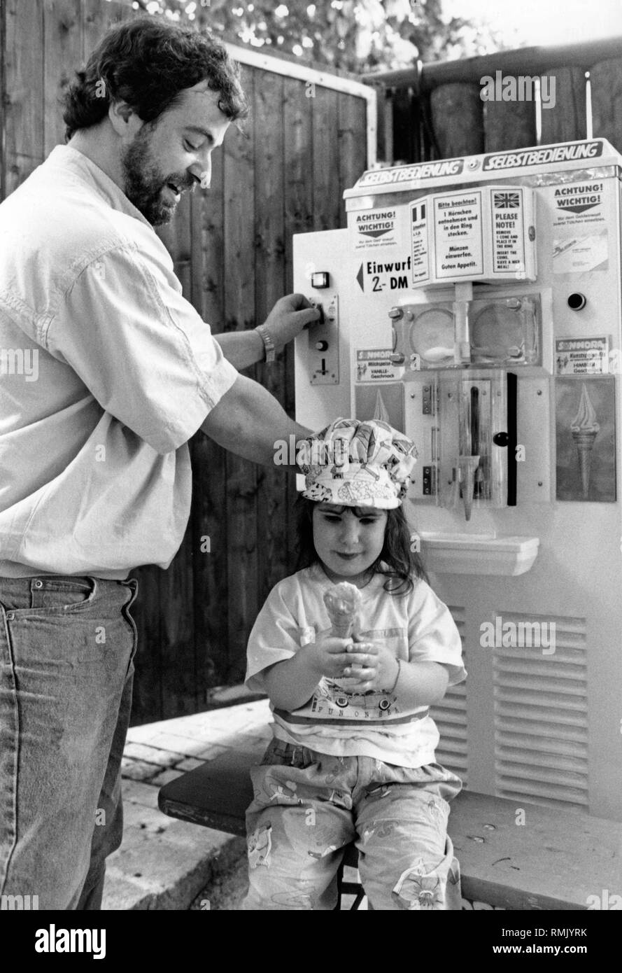 Tanja avec son père en face d'un self-service machine à crème glacée molle. Tandis que la fille est déjà en possession de sa glace dans sa main, le père jette des pièces de monnaie dans la machine pour un autre service de la crème glacée. Banque D'Images