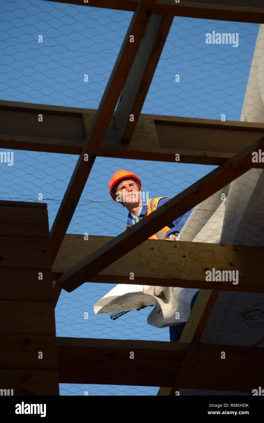 Un constructeur marteaux vers le bas du papier de construction, alors que l'équipe met la toiture d'un grand immeuble commercial Banque D'Images