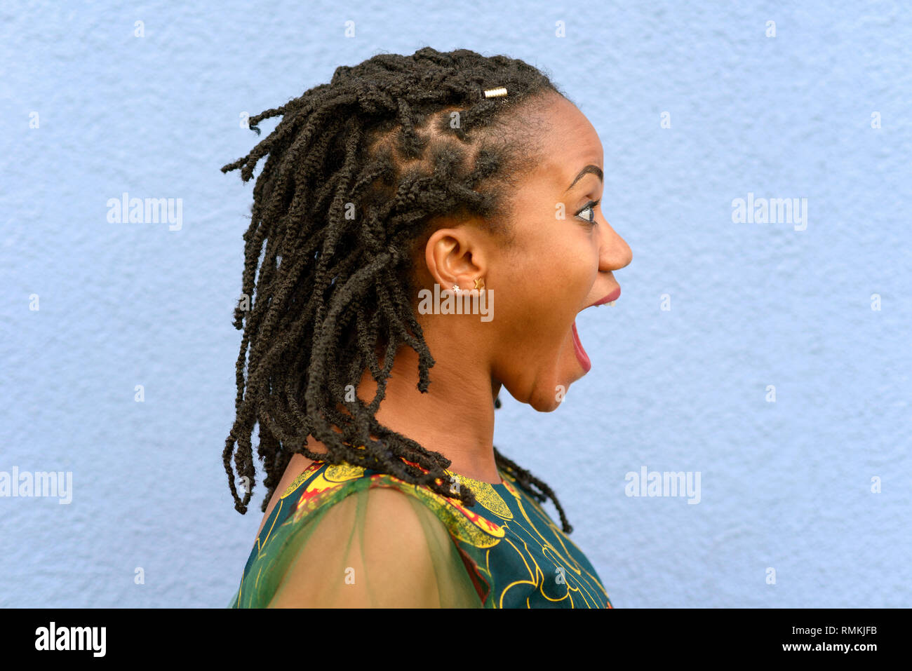 Heureux surpris jeune femme africaine avec des dreadlocks tressés fixant l'avant avec de grands yeux et bouche ouverte plus de bleu dans le profil Voir Banque D'Images
