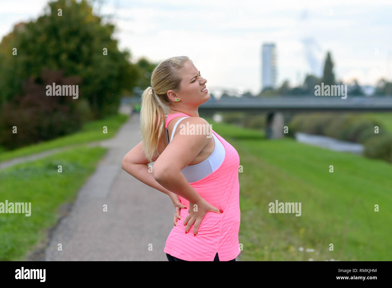 Young blonde woman wearing sportswear tenant son dos douloureux tout en exerçant à l'extérieur Banque D'Images