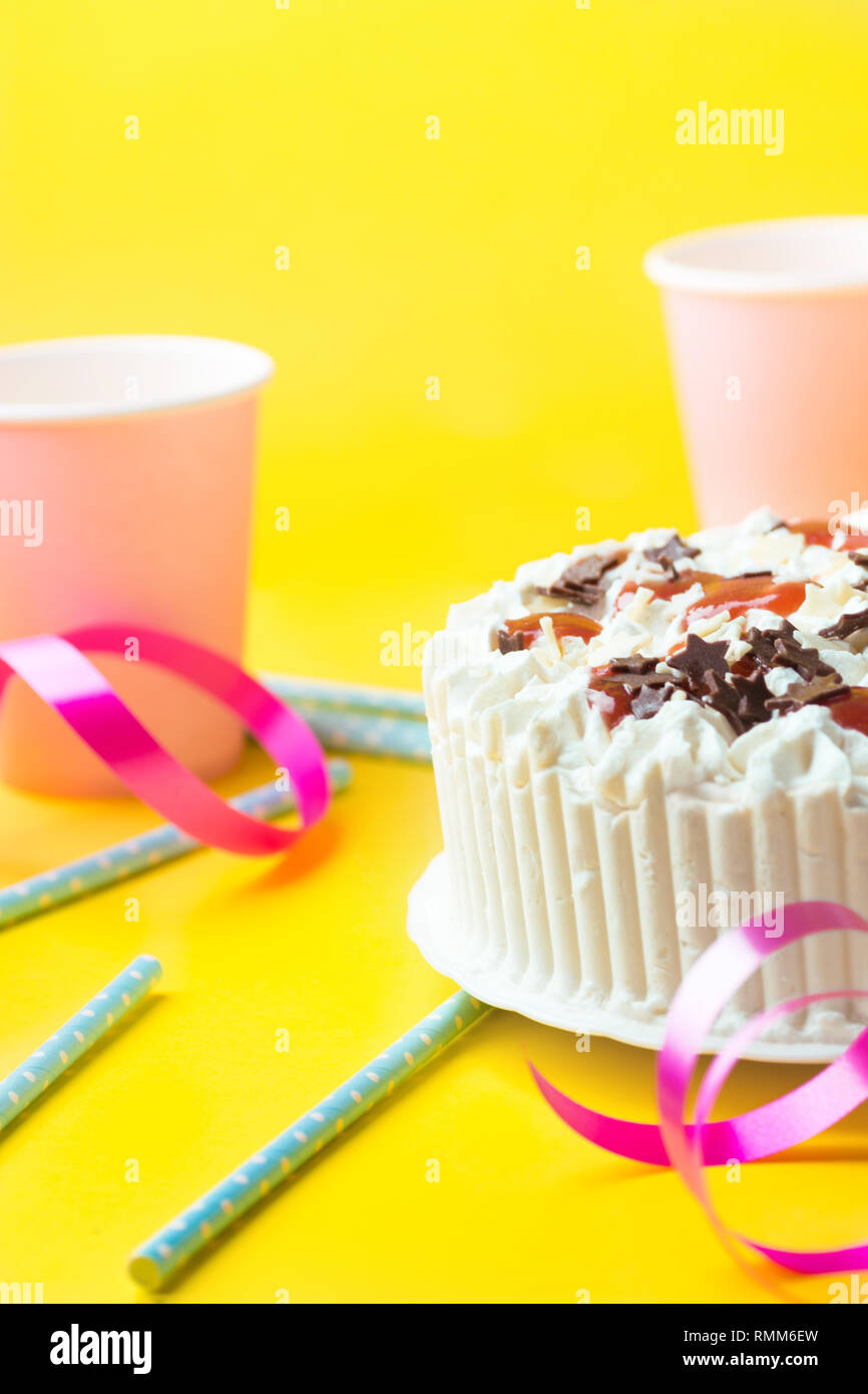 Couche éponge gâteau d'anniversaire avec de la crème chantilly au chocolat au lait glaçage star nutrifer confiture de fraises. Gobelets en papier rose paillettes bleu ruban frisé Banque D'Images