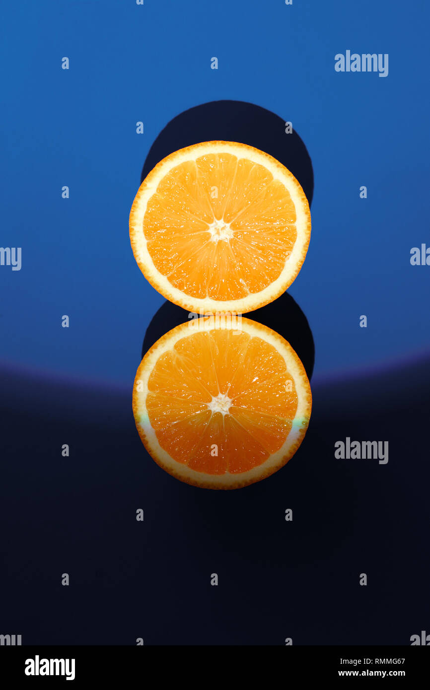 Les deux moitiés d'orange mûre sur un fond bleu en plein soleil . Banque D'Images