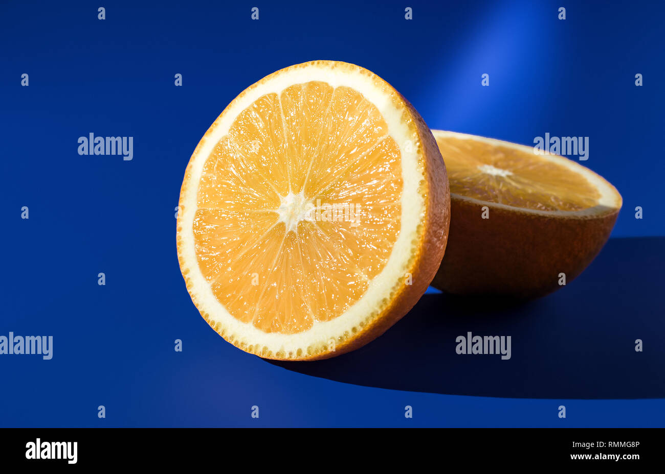 Les deux moitiés d'orange mûre sur un fond bleu en plein soleil . Banque D'Images