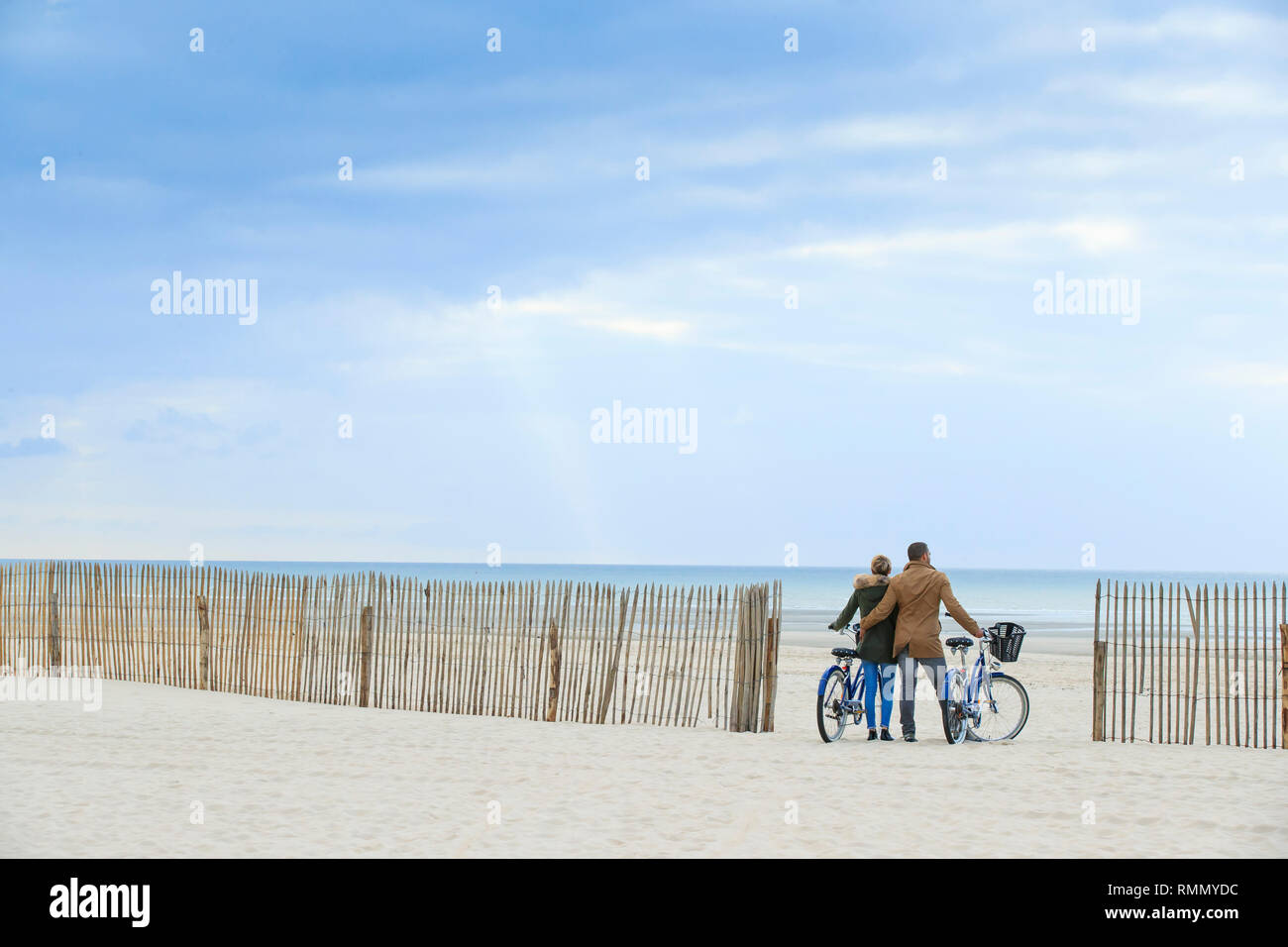Couple riding bikes sur la plage du Touquet en hiver. Vue de derrière le couple face à la mer et ganivelles, barrières en bois utilisés pour stabiliser Banque D'Images