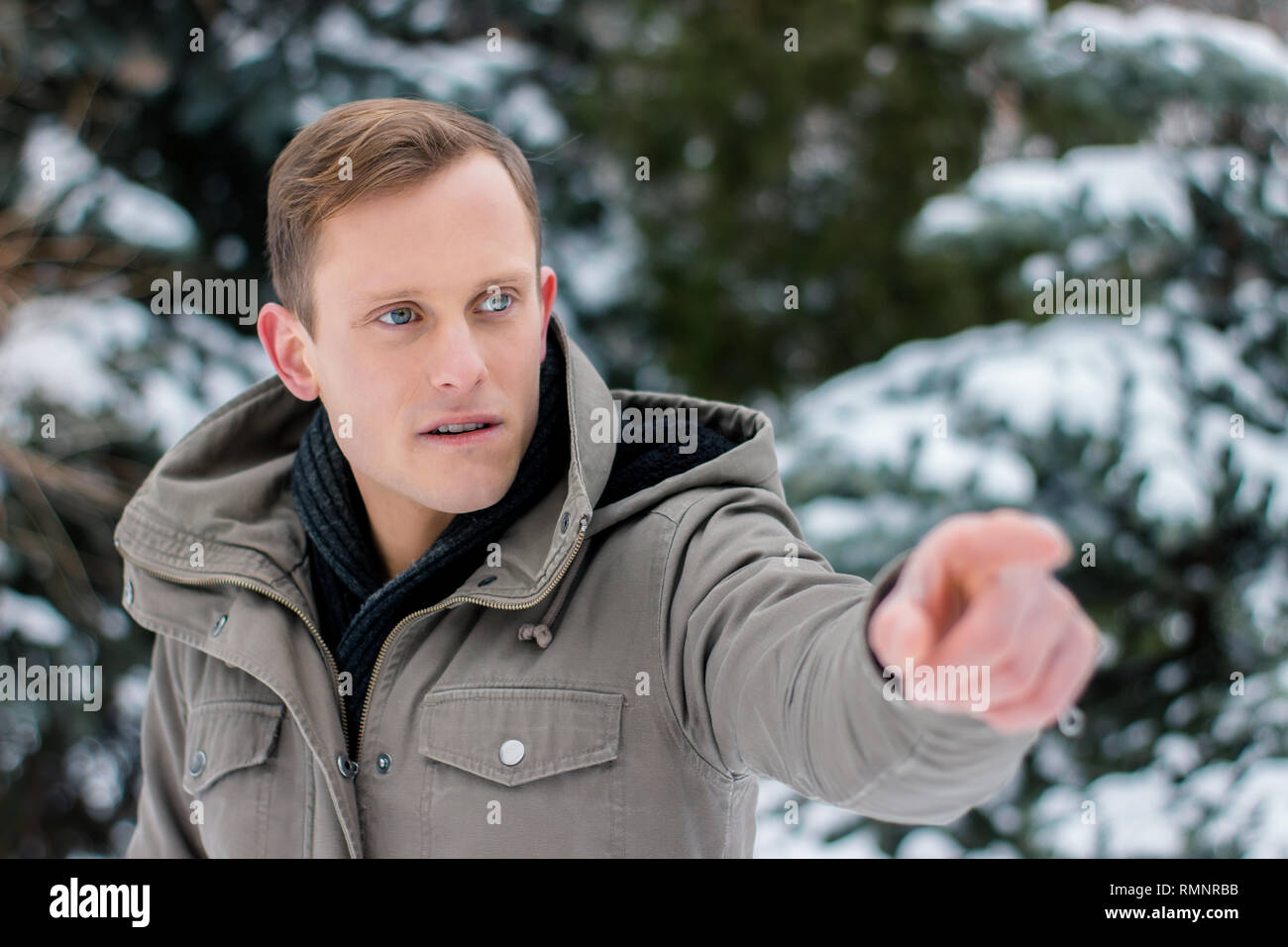 Un jeune homme dans un paysage d'hiver indique la direction de sa main gauche Banque D'Images