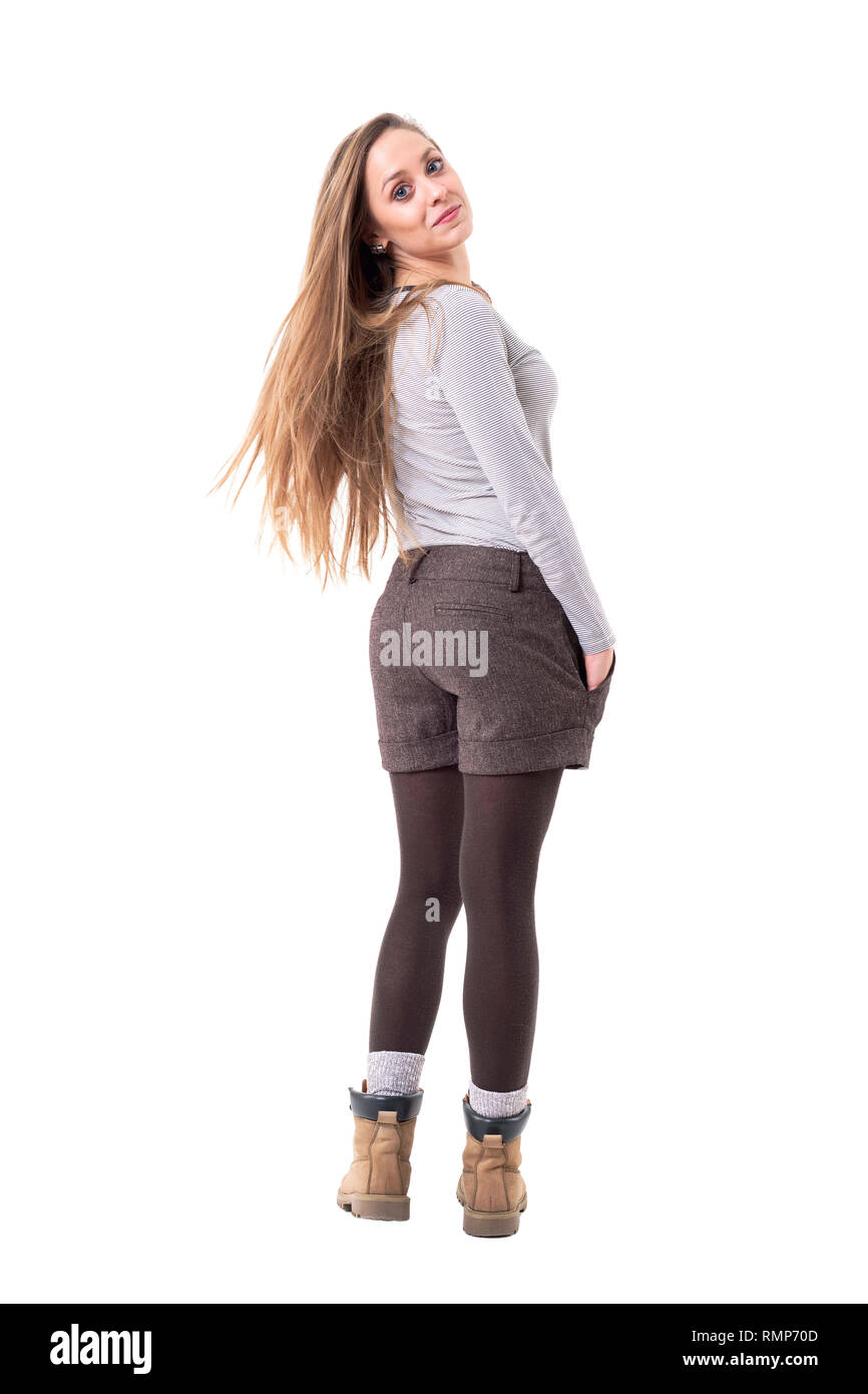 Vue arrière de l'heureuse jeune fille enjouée hipster avec de longs cheveux blonds et tournant à retour à l'appareil photo. Corps plein isolé sur fond blanc. Banque D'Images