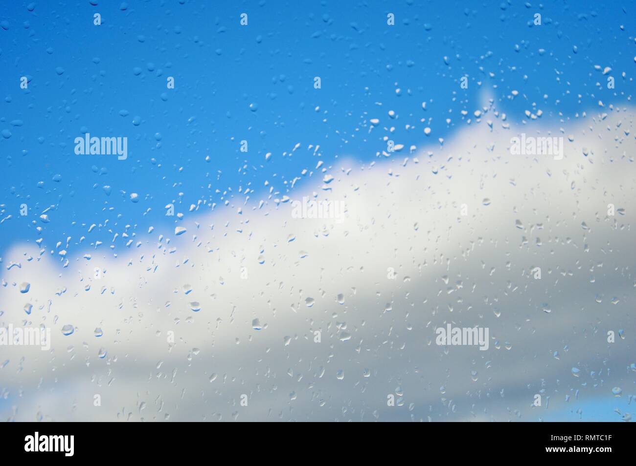 Fenêtre avec des gouttes de pluie contre un ciel bleu avec des nuages blancs après une tempête au milieu de l'hiver. Changement de temps.Le temps efface.Les gouttes de stick à la fenêtre Banque D'Images