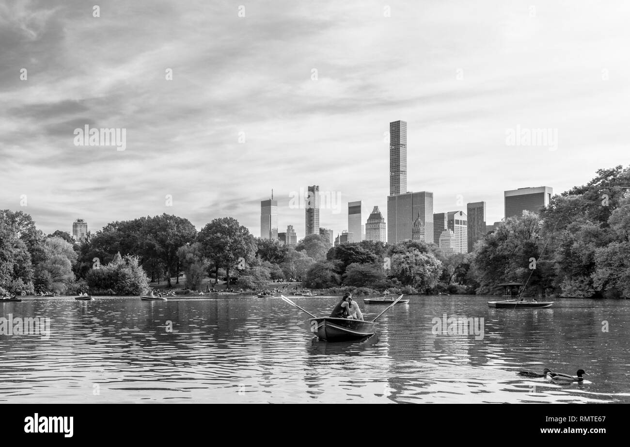 Couple dans une chaloupe sur le lac de Central Park avec le Mid Town Manhattan sous filandreux nuages à l'horizon, noir et blanc. Banque D'Images