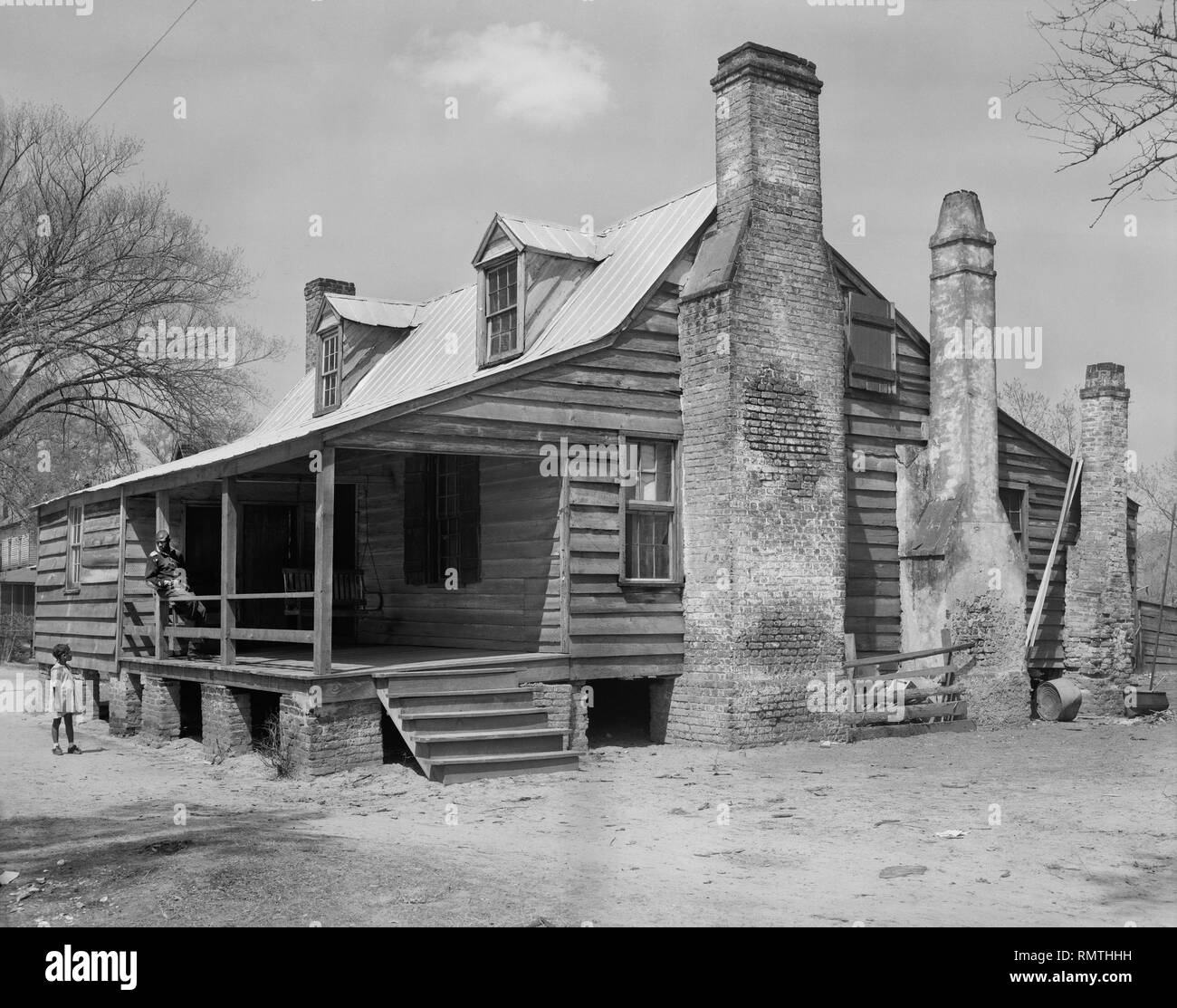 Homme assis sur le perron de la maison en bois tout en jeune fille se tient dans la cour avant, Georgetown, Caroline du Sud, USA, Frances Benjamin Johnston, 1937 Banque D'Images