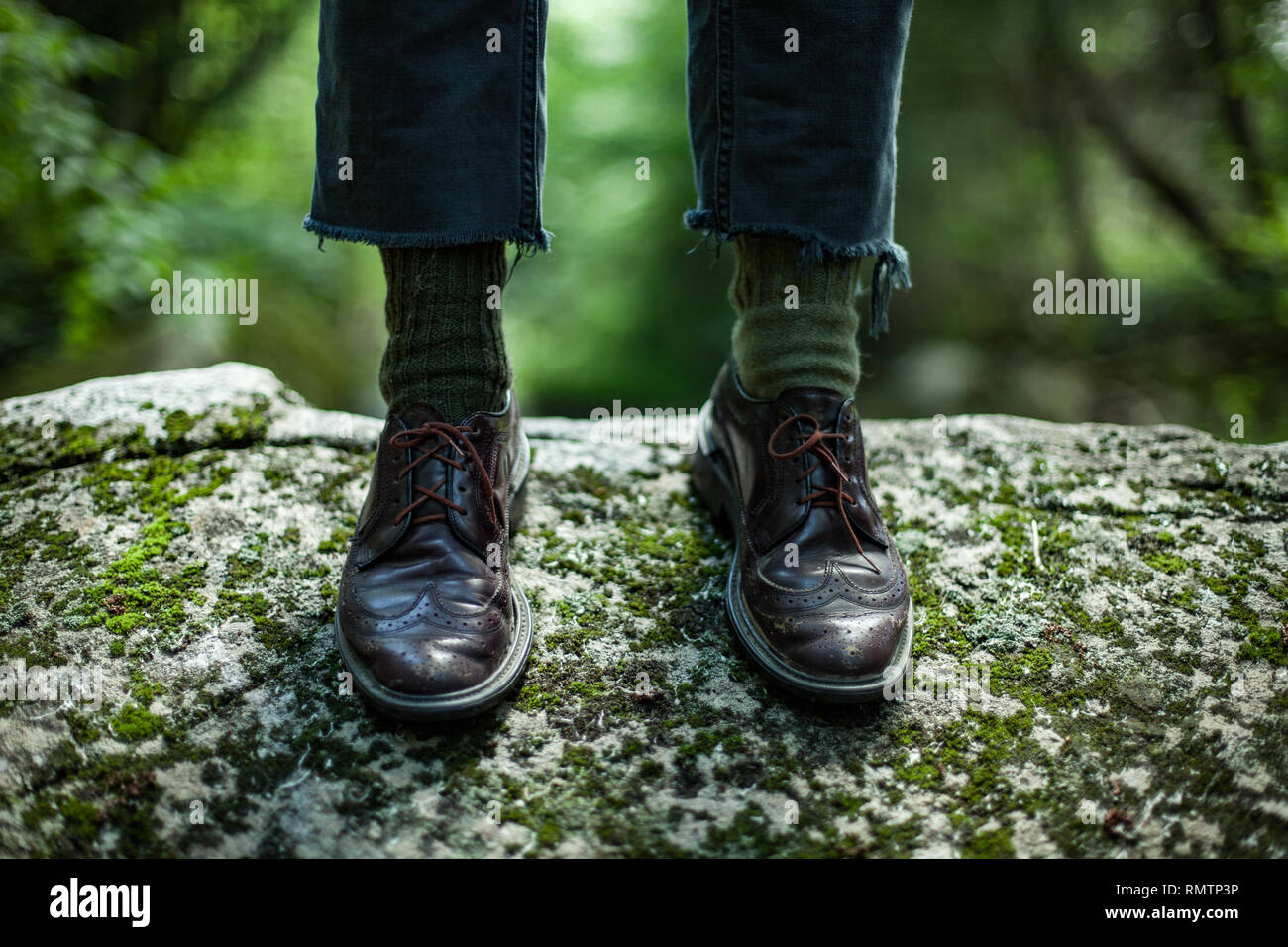Les pieds de l'homme portant des chaussures en cuir et des chaussettes vert, debout sur un rocher avec un arrière-plan flou de la nature Banque D'Images