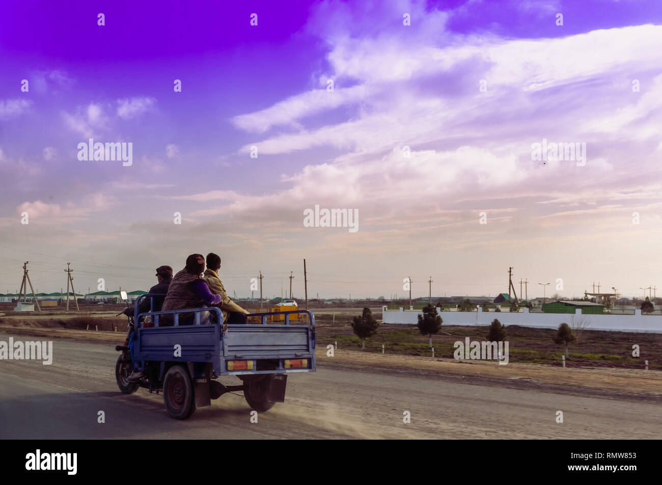 Trois personnes, un conducteur d'une moto et deux autres placés sur un chariot à l'arrière de la conduite sur une route dans l'après-midi. Blue cloudy sky sur l'arrière Banque D'Images