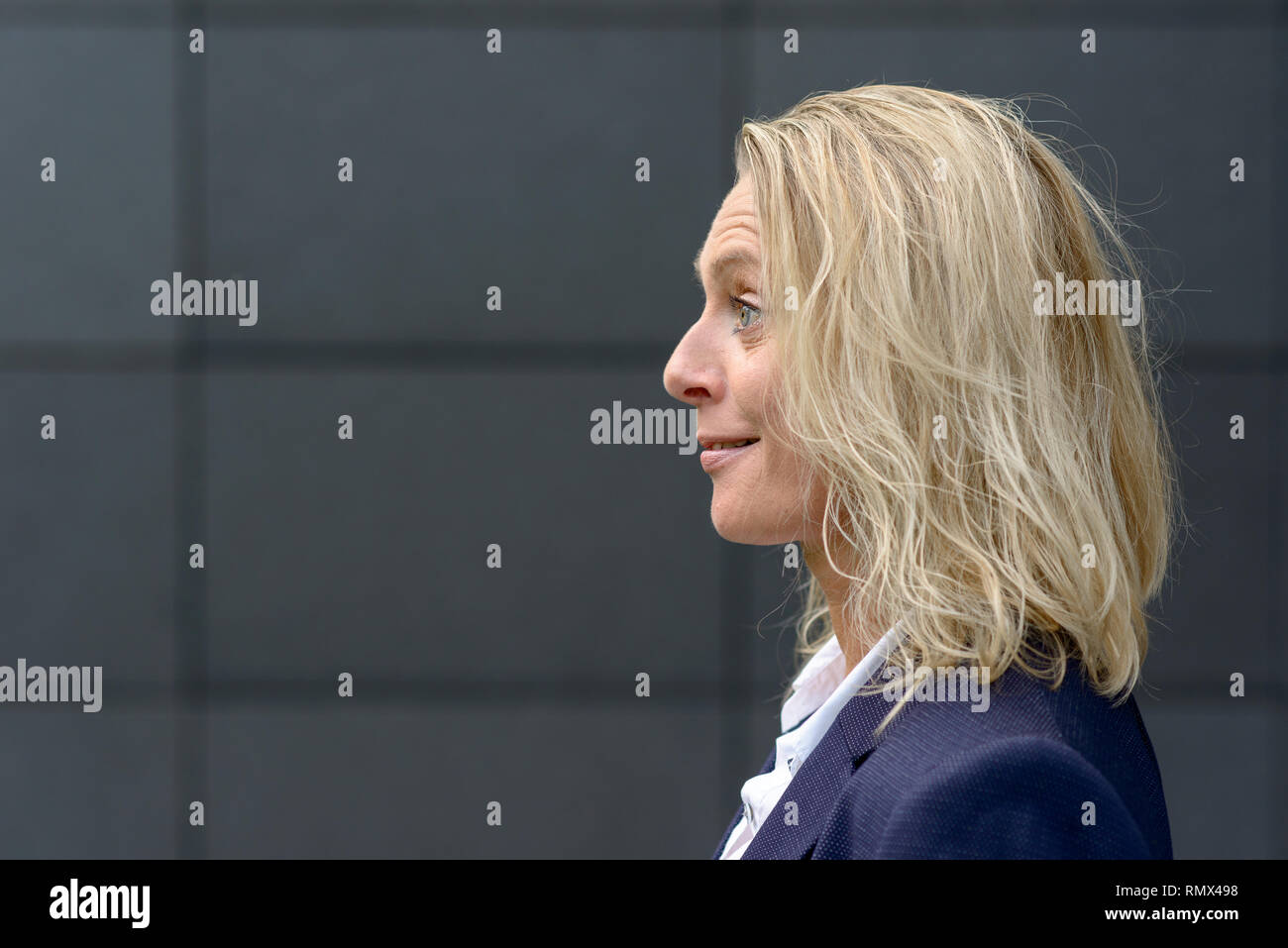 Head shot Profil d'une femme blonde surpris avec les cheveux ébouriffés de sourire et élever ses sourcils avec copie espace sur un mur gris foncé Banque D'Images