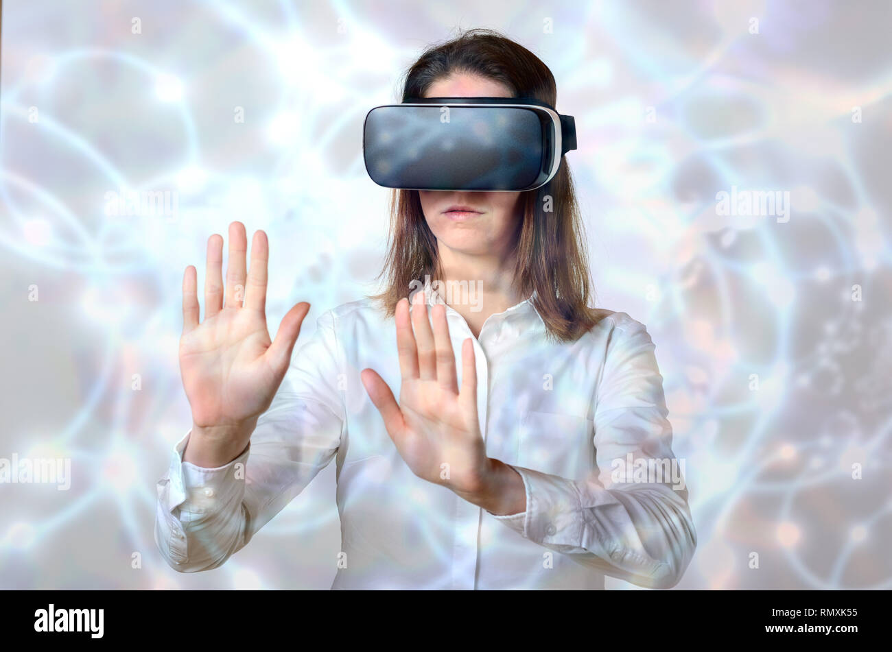 Femme en chemise blanche se tripoter les objets invisibles dans la réalité virtuelle avec ses deux mains, debout dans le noir contre des lunettes 3D abstrait arrière-plan lumineux Banque D'Images