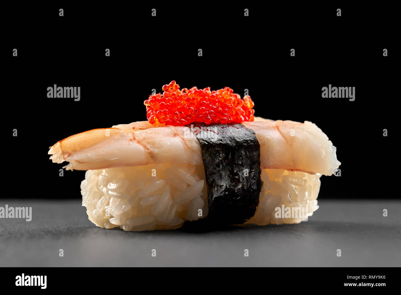 Ebi nigiri sushi sur plaque de pierre noire. Riz aux crevettes, enveloppé dans une bande de nori et surmontée d'oeufs de poisson volant rouge. Banque D'Images