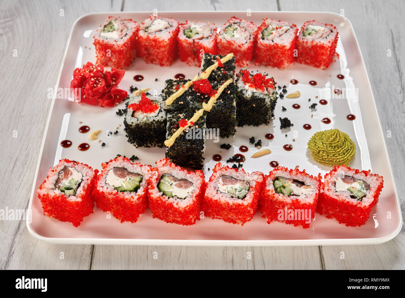 Plaque blanche avec rouleaux de sushi japonais, décoré de mayo, wasabi et gingembre mariné. Uramaki Philadelphie rempli de saumon, de concombre, de fromage à la crème, recouvert de tobiko re. Banque D'Images