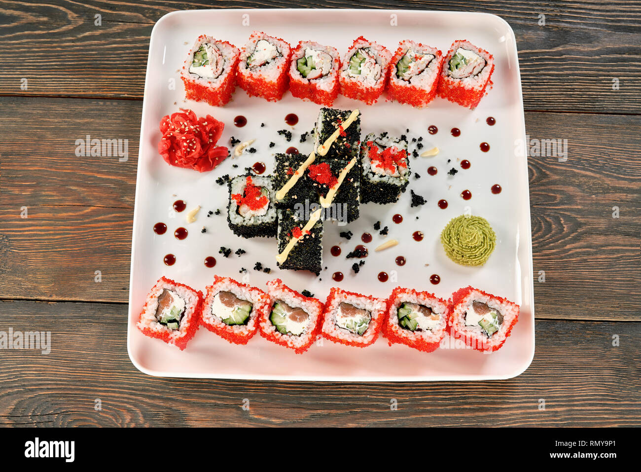 Rouleaux de Philadelphie avec le saumon, le fromage à la crème et le concombre. Sushi Uramaki décoré avec Mayo, wasabi et gingembre mariné, couvert de tobiko rouge, présenté le re plaque blanche. Banque D'Images