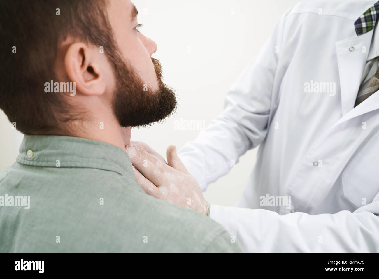 Close up portrait homme barbu de face sur l'examen médical. Docteur en médecine, blanc de toucher le cou, palpation, uniforme et d'examiner les ganglions lymphatiques. Patient sur consultation avec le thérapeute. Banque D'Images
