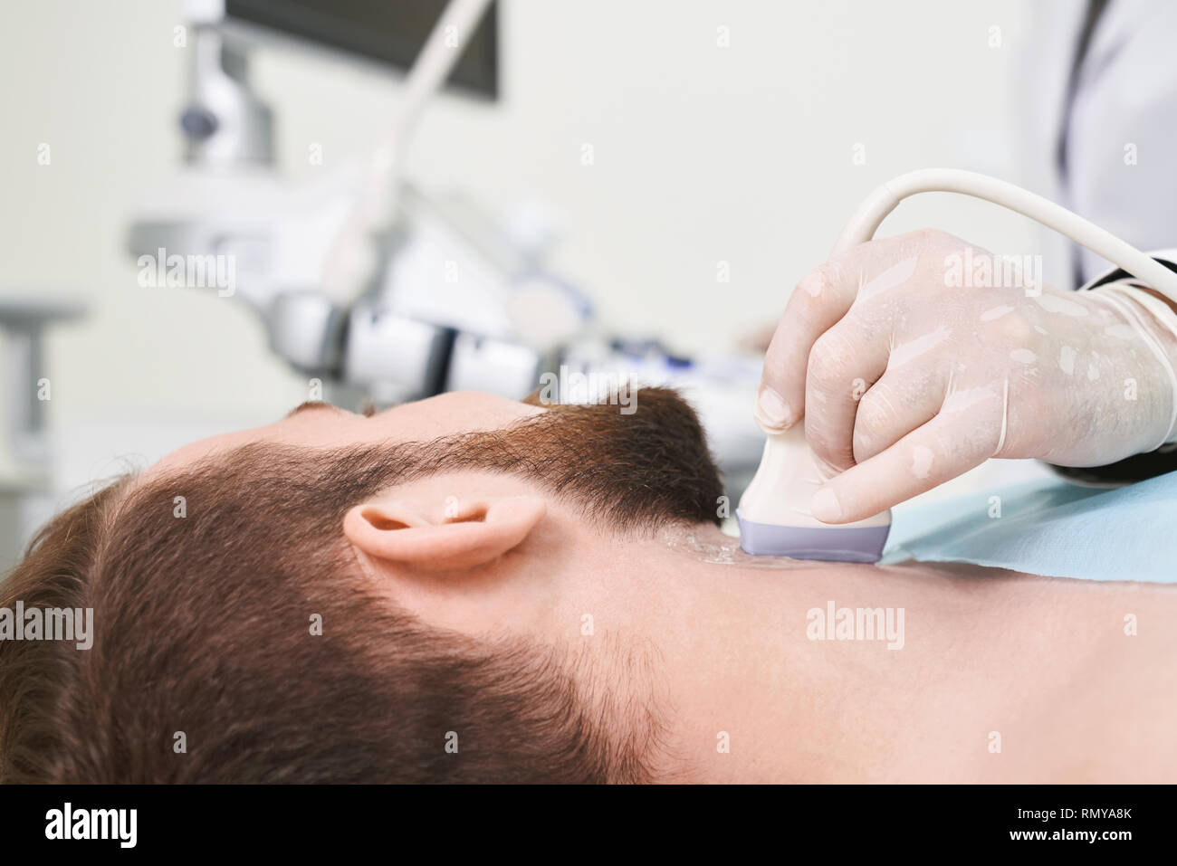 Close up de tête d'homme barbu, patient lying in medical office. Main de médecin en blanc, la tenue des gants médicaux, sonde à ultrasons et l'examen des ganglions du cou. Banque D'Images