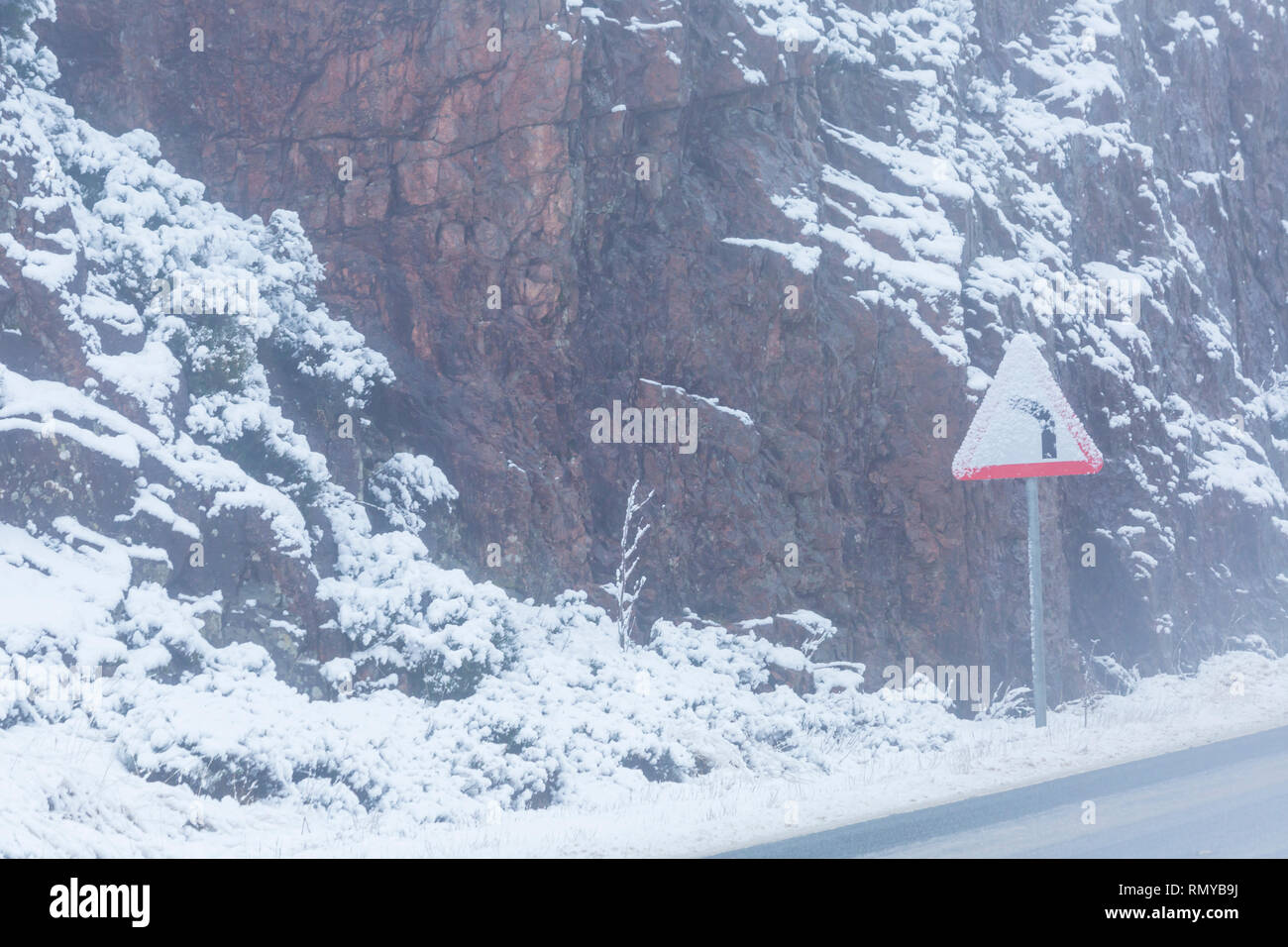 Plier au panneau de gauche dans la neige sur la route A82 sur un froid matin d'hiver à Rannoch Moor, Argyll, Écosse en janvier - triangle de signalisation de route triangulaire Banque D'Images