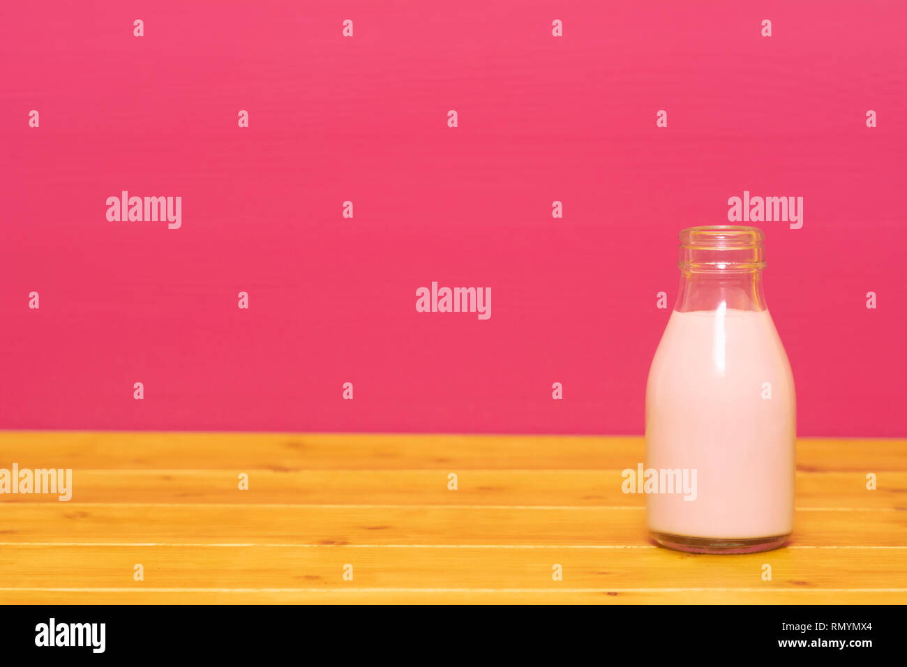 Lait frappé aux fraises dans un tiers de pinte de lait, bouteille en verre sur une table en bois contre un arrière-plan peint rose Banque D'Images