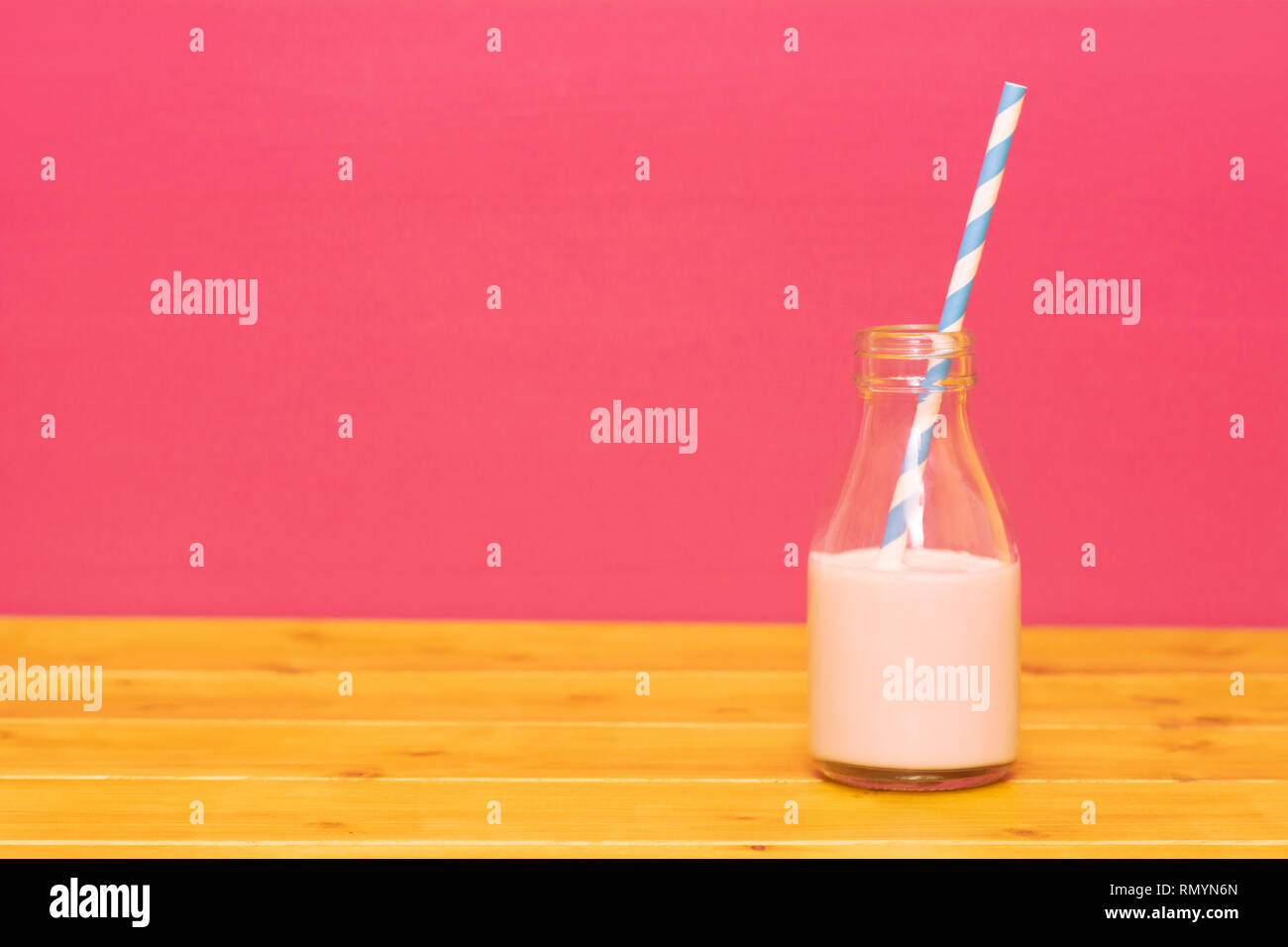 Un tiers de pinte de lait en verre bouteille à moitié plein d'un milkshake à la fraise avec paille papier rétro, sur une table de bois contre un fond rose Banque D'Images