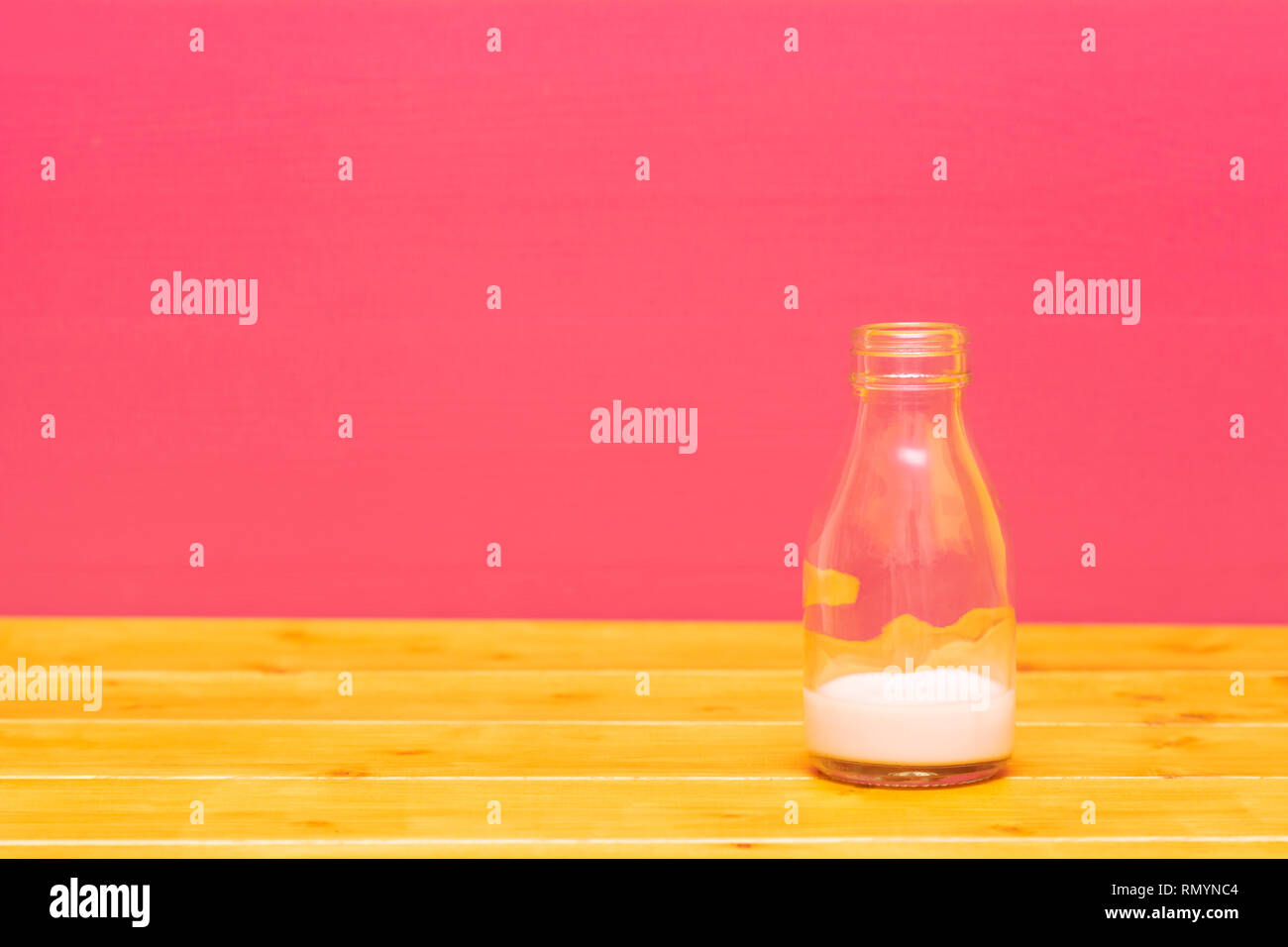 Un tiers de pinte de lait en verre bouteille avec lie de strawberry milkshake, sur une table de bois contre un arrière-plan peint rose Banque D'Images