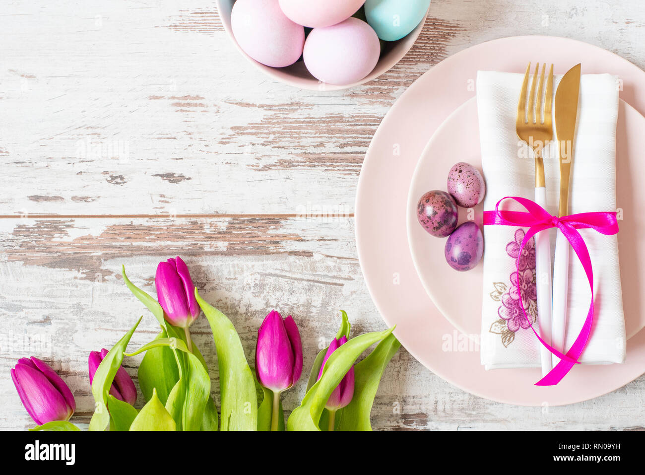 Réglage de la table de Pâques, flatlay avec les oeufs de pâques aux couleurs pastel, la décoration de l'événement. Or rose typiques et une fourchette et une cuillère sur une lumière arrière en bois rustique Banque D'Images