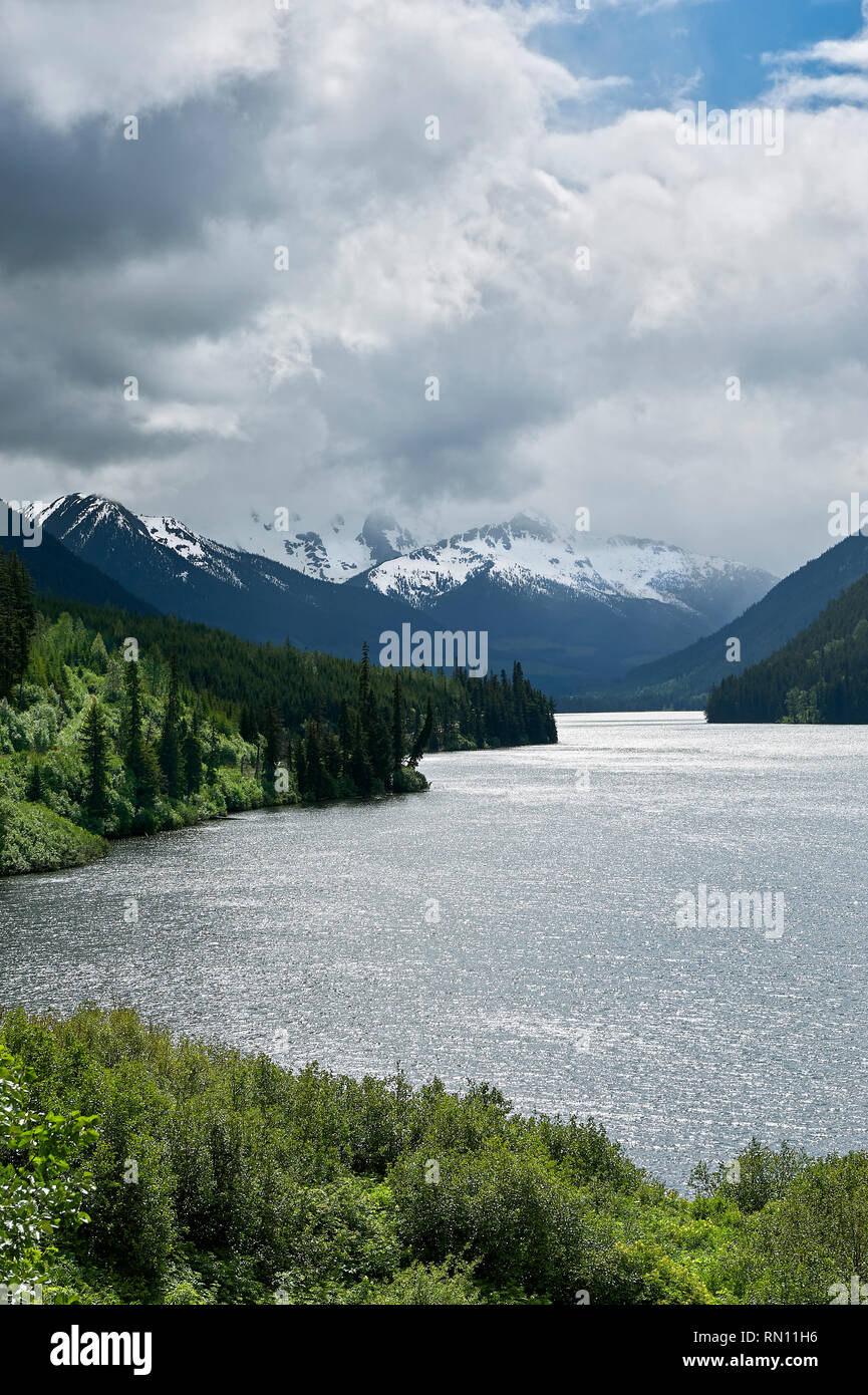 Voir au lac Duffey, avec ciel couvert au-dessus des montagnes enneigées, entouré de forêt, le long de la route 99, près de Whistler, British Columbia, Canada Banque D'Images